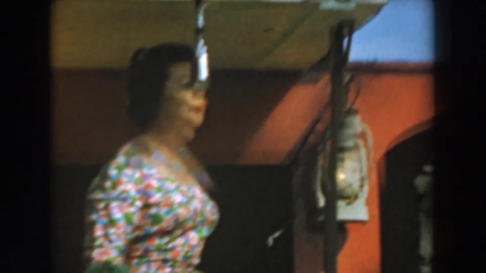 Side view of the performer at Knott's Berry Farm, with a suspended microphone, red wall, and lantern visible in the 8mm frame.