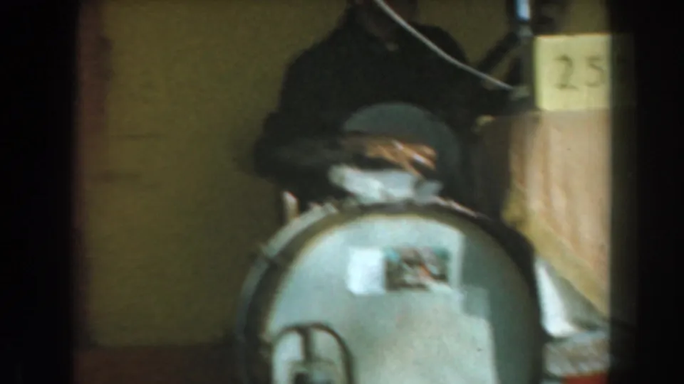 1961 Knott's Berry Farm home-movie frame showing a dim interior with a round metal object, a partially visible person, and a numbered box.