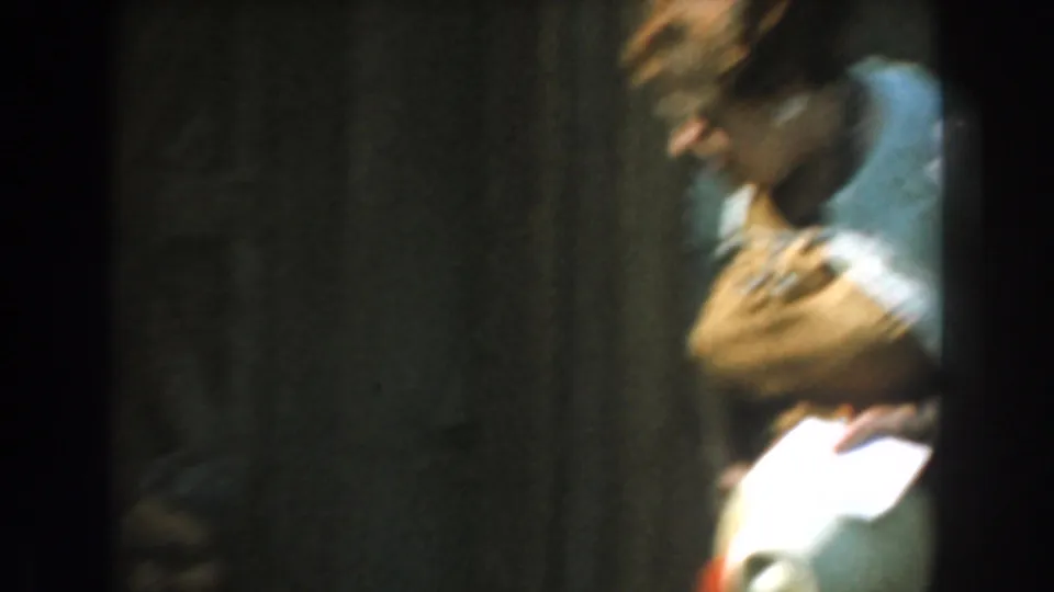 1961 Knott's Berry Farm home-movie frame showing a person in a light shirt leaning forward in a shadowed hall interior.