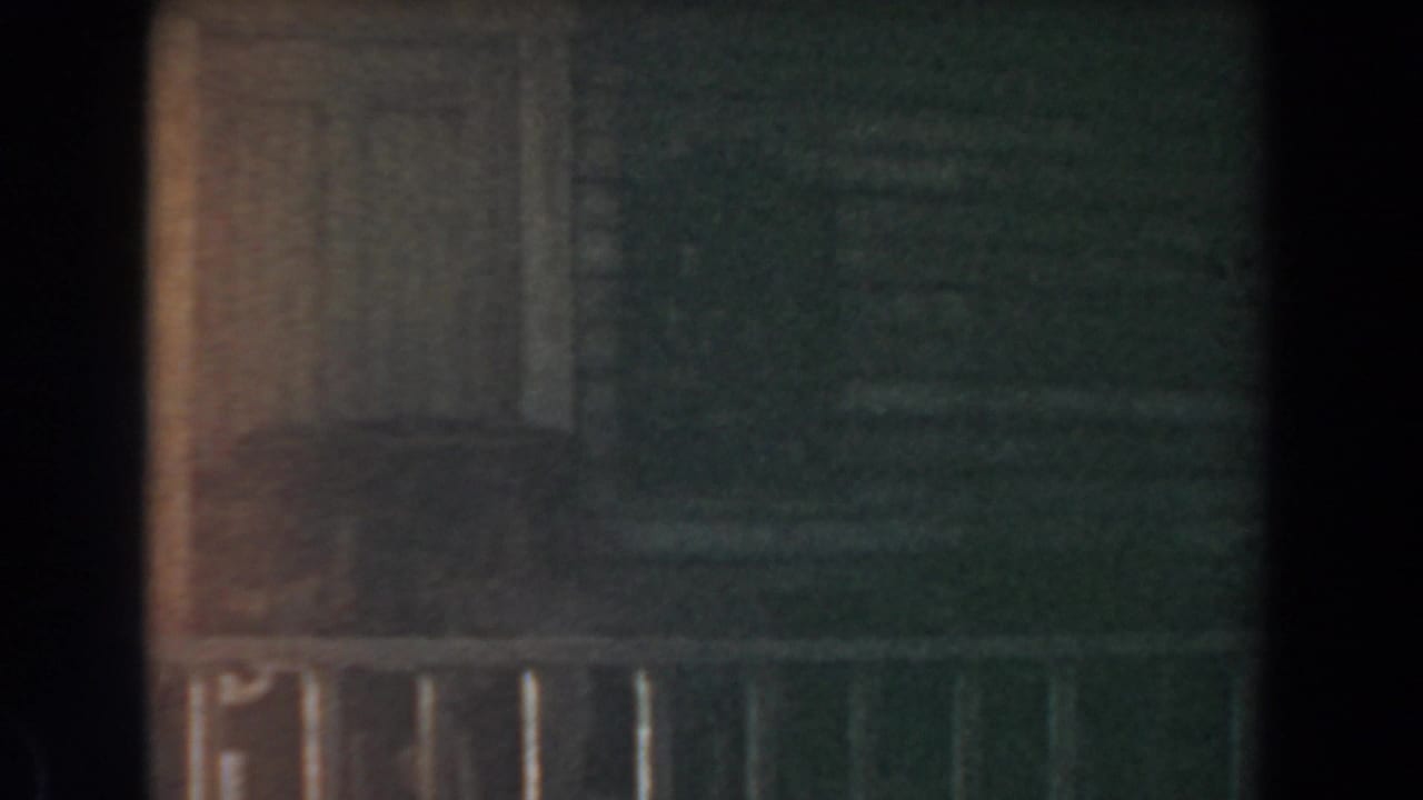 Low-light 1961 Knott's Berry Farm frame with a rustic wall, pale door or shutter, railing, and greenish shadow.