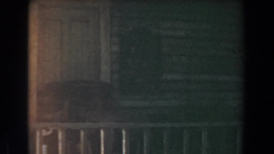 Low-light 1961 Knott's Berry Farm frame with a rustic wall, pale door or shutter, railing, and greenish shadow.