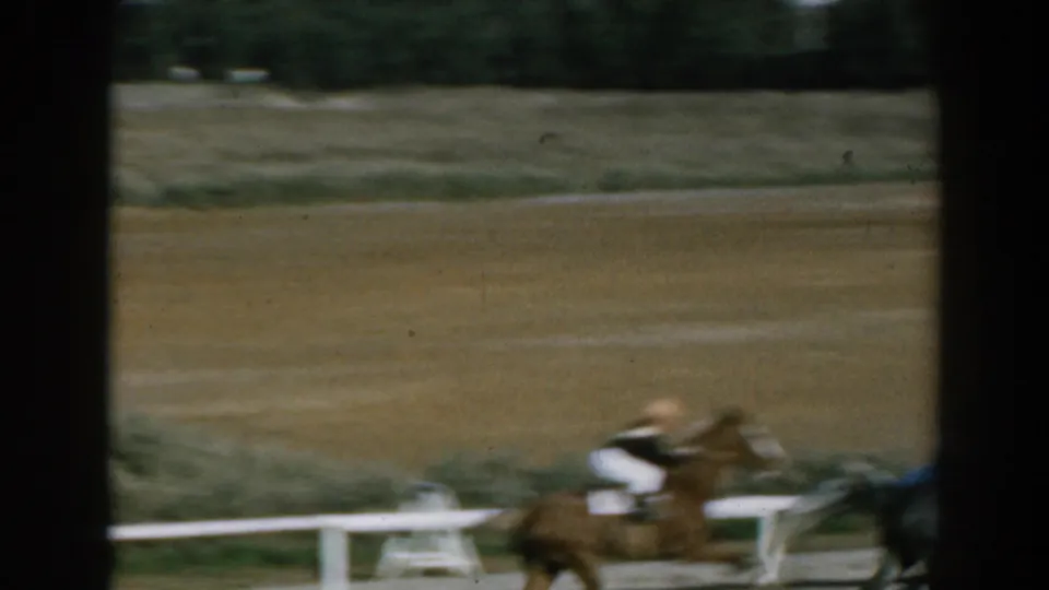A close, motion-blurred view shows a horse and jockey passing the camera on the dirt track in 1962 Greece footage.