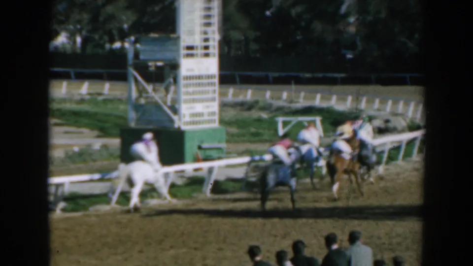 Racehorses and jockeys gather or pass near a starting gate, with spectators visible in the foreground of the 1962 Greece racetrack scene.