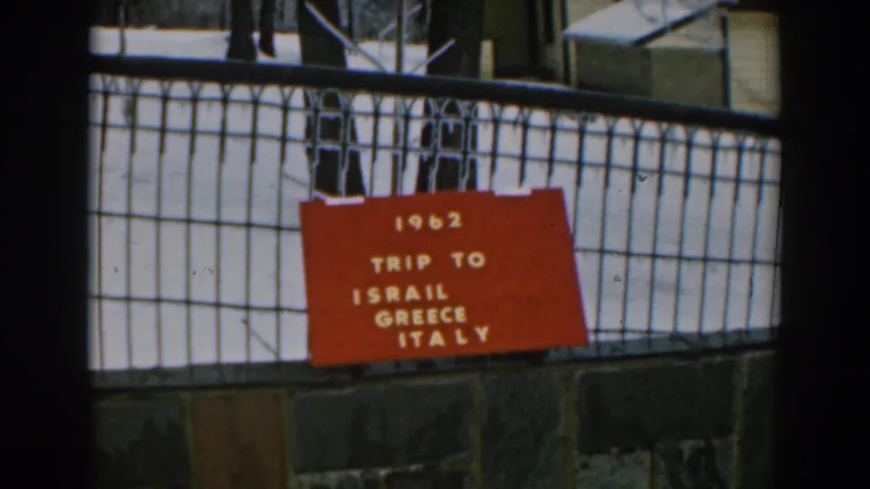 8mm frame of a red 1962 trip board on a black metal fence, with winter ground visible beyond.