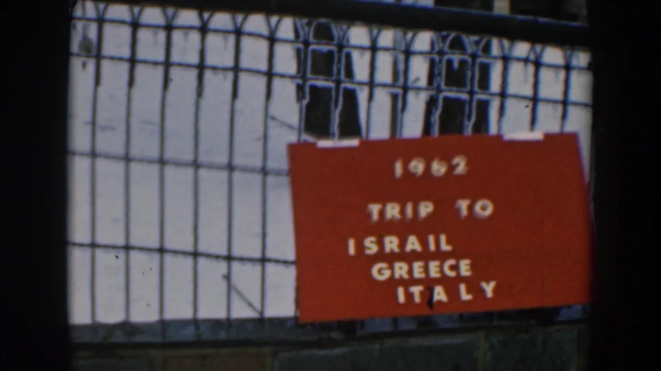Red 1962 trip title card on a black fence, with white text naming Israel, Greece, and Italy.