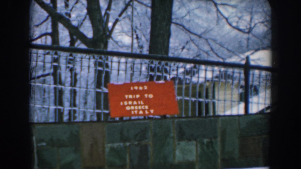 Red travel sign on a fence above a stone wall in a snowy wooded setting.