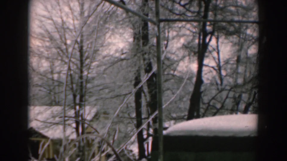 1962 Greece home-movie frame with snow on a roof, bare trees, and a pale winter sky seen through dark vertical framing.