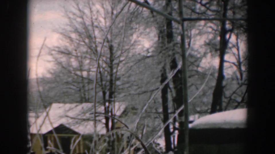 1962 Greece 8mm frame showing bare trees, a snow-covered roofline, and a soft winter hillside beyond.