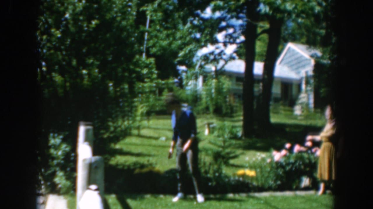 Woman in a blue shirt stands in a green garden near flowers and trees.