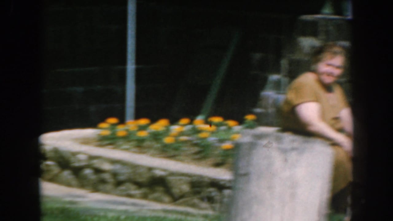 Woman seated on a low garden wall beside orange flowers and stonework.