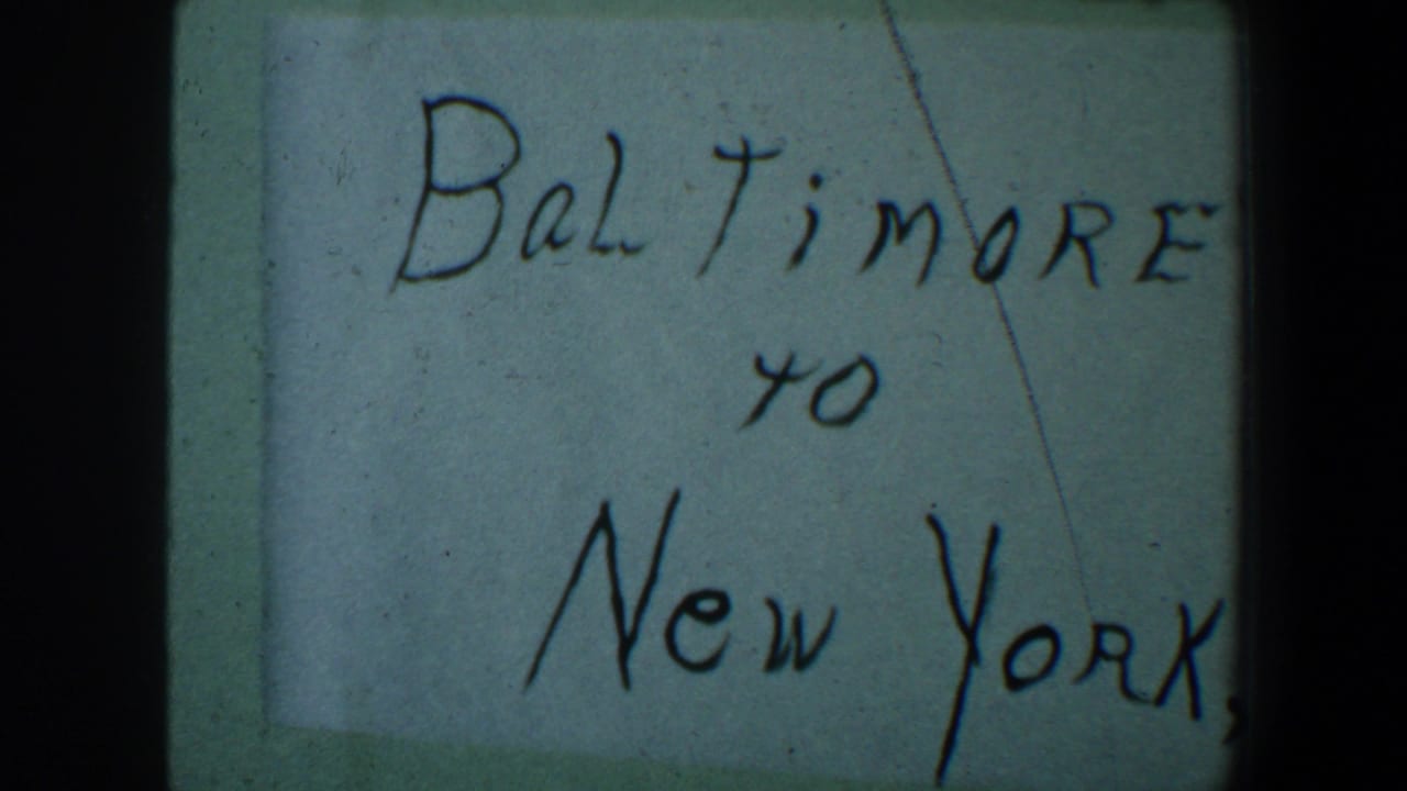 1960 8mm frame showing a handwritten Baltimore to New York travel note on pale paper with visible film borders.