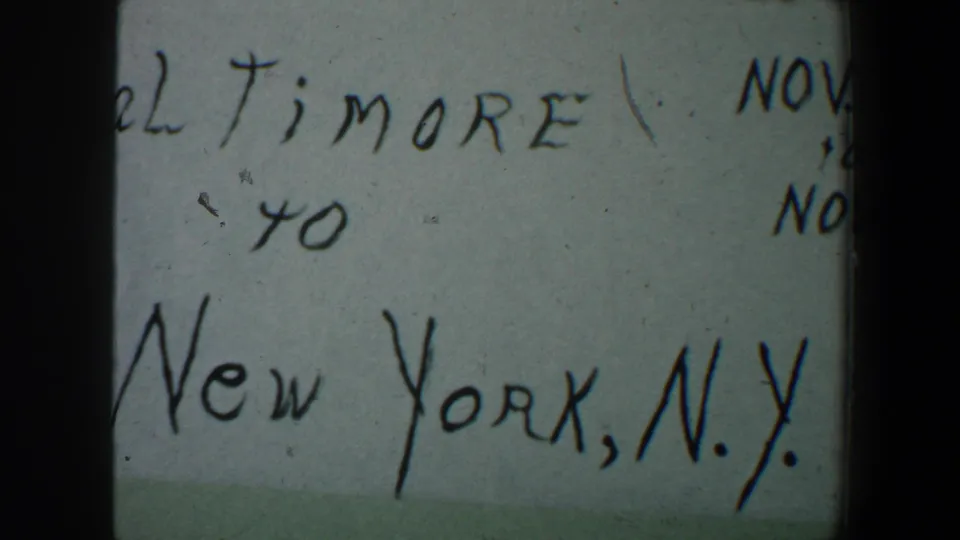 1960 8mm frame showing a cropped handwritten Baltimore to New York, N.Y. travel note with visible film texture.