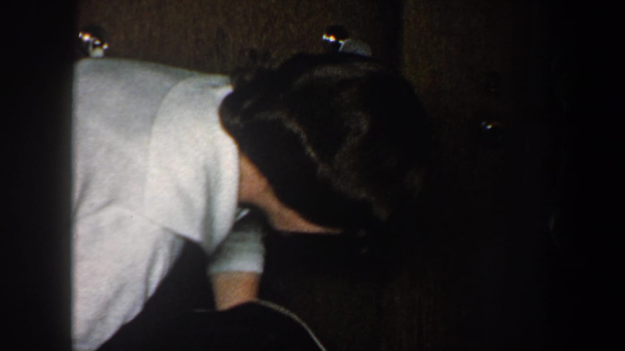 Adult in a light shirt leans down near another person in shadow.