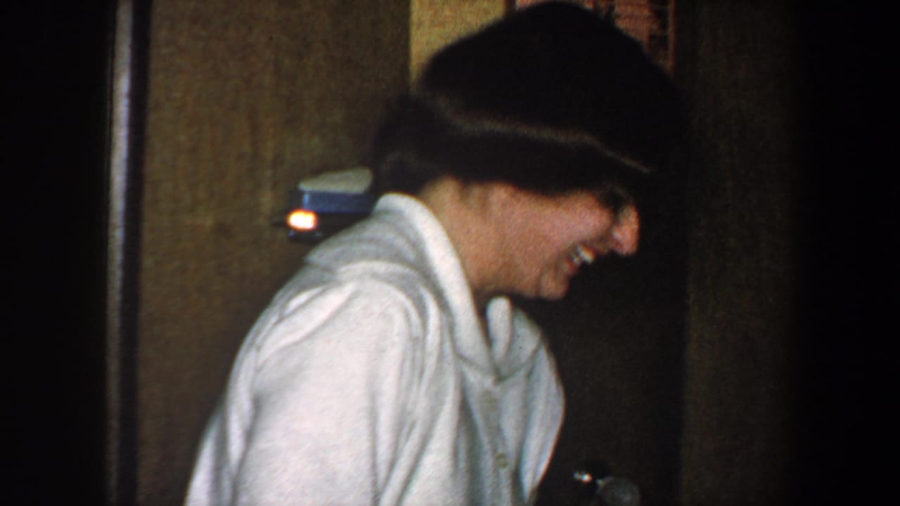 Woman in a light shirt laughs in profile near a wood door.