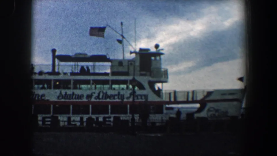 1960 New York City frame of the Statue of Liberty Ferry at a harbor dock, with Circle Line markings, flags, and small passenger figures on deck.