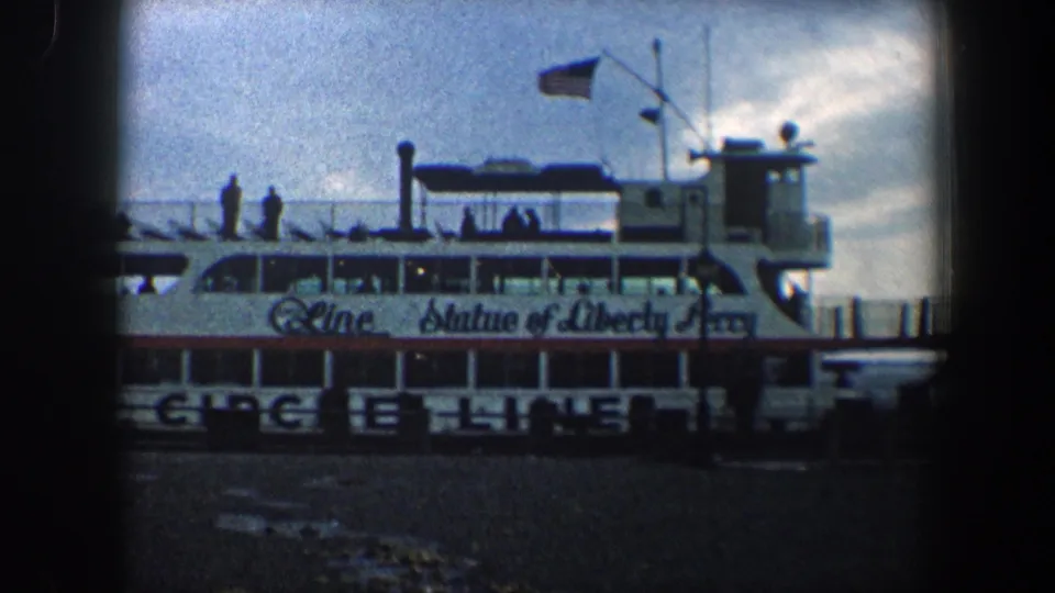 1960 New York City home-movie frame showing the ferry midsection, with Circle Line text, Statue of Liberty Ferry lettering, passengers, and flags.