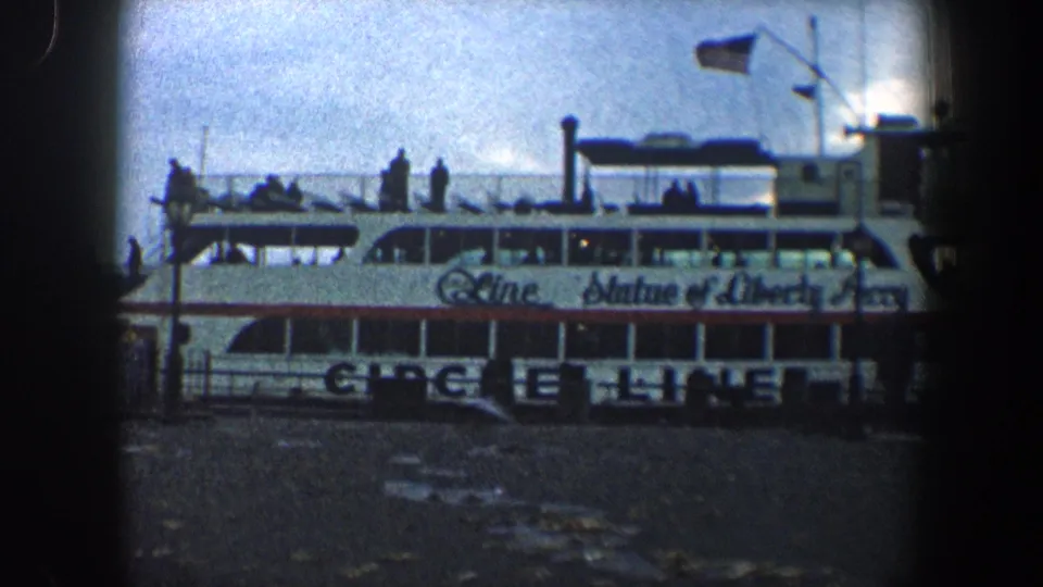 1960 New York City 8mm frame showing more of the Statue of Liberty Ferry side, upper-deck passengers, Circle Line markings, railings, and vignetted edges.