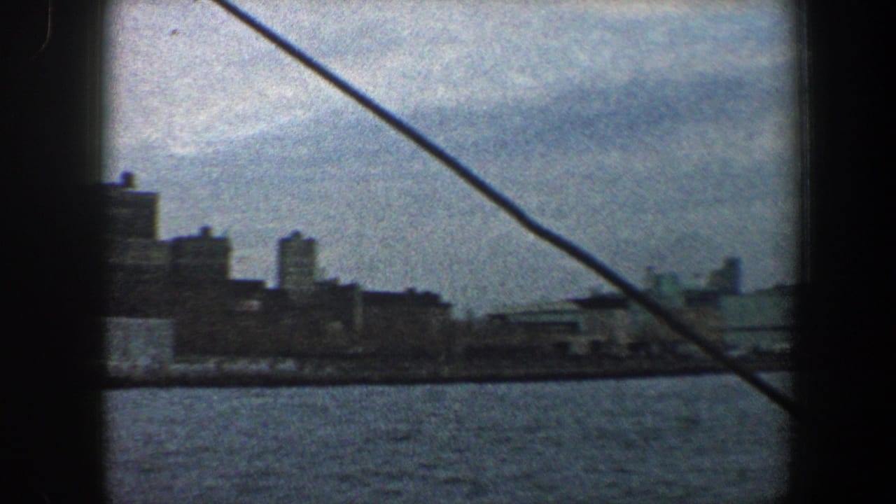 1960 New York City skyline and waterfront viewed from a boat, with diagonal rope or cable crossing the frame.