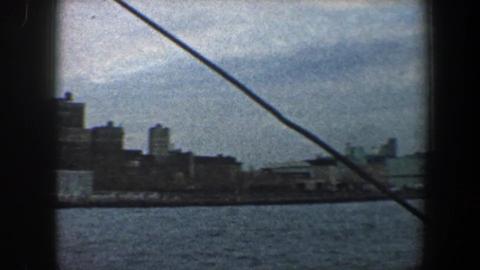 1960 New York City skyline and waterfront viewed from a boat, with diagonal rope or cable crossing the frame.