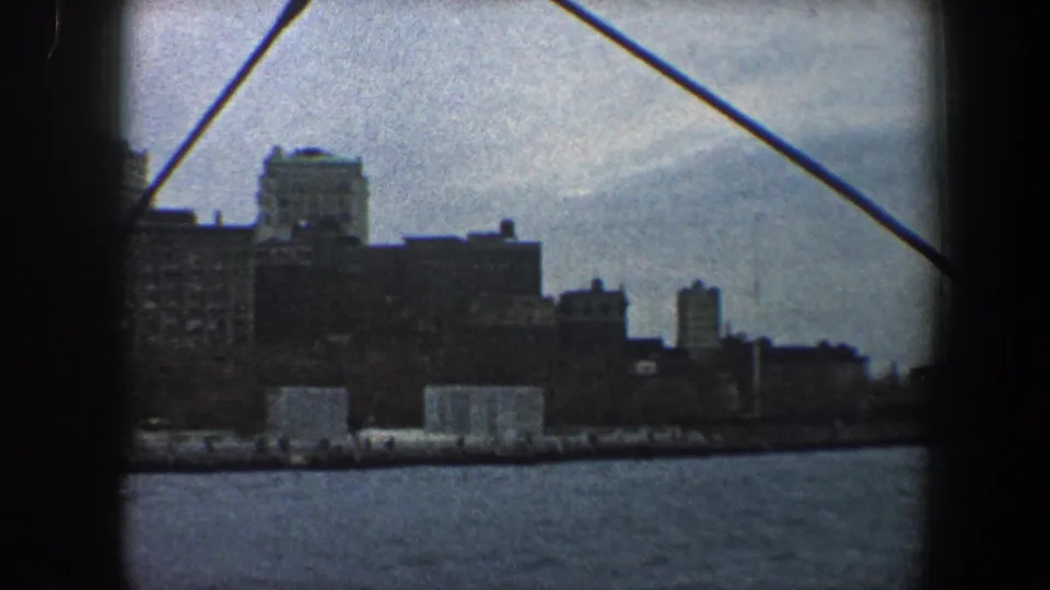 New York City waterfront buildings seen from the water in 1960, partly obscured by boat structure and cable.
