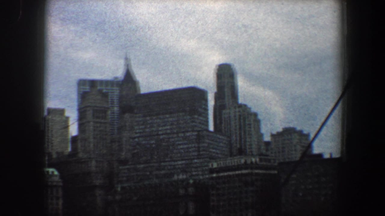 1960 8mm view of the New York City skyline with clustered high-rises, a spired tower form, and dark film borders.