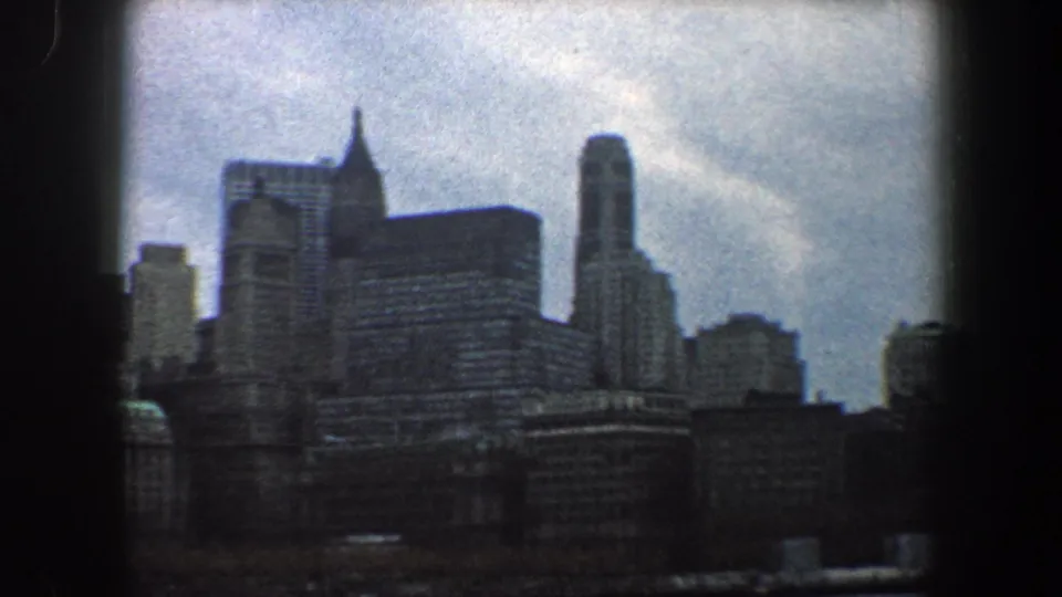1960 8mm skyline view of New York City, showing a broad dark building mass, tall rounded tower, and cloudy daylight sky.