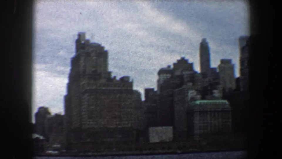 A continued 8mm pan across New York City shows tall waterfront buildings under overcast light.