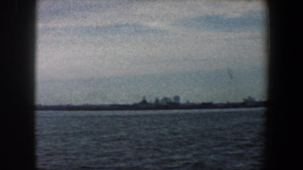 Distant harbor horizon with low buildings across dark water under a cloudy sky.