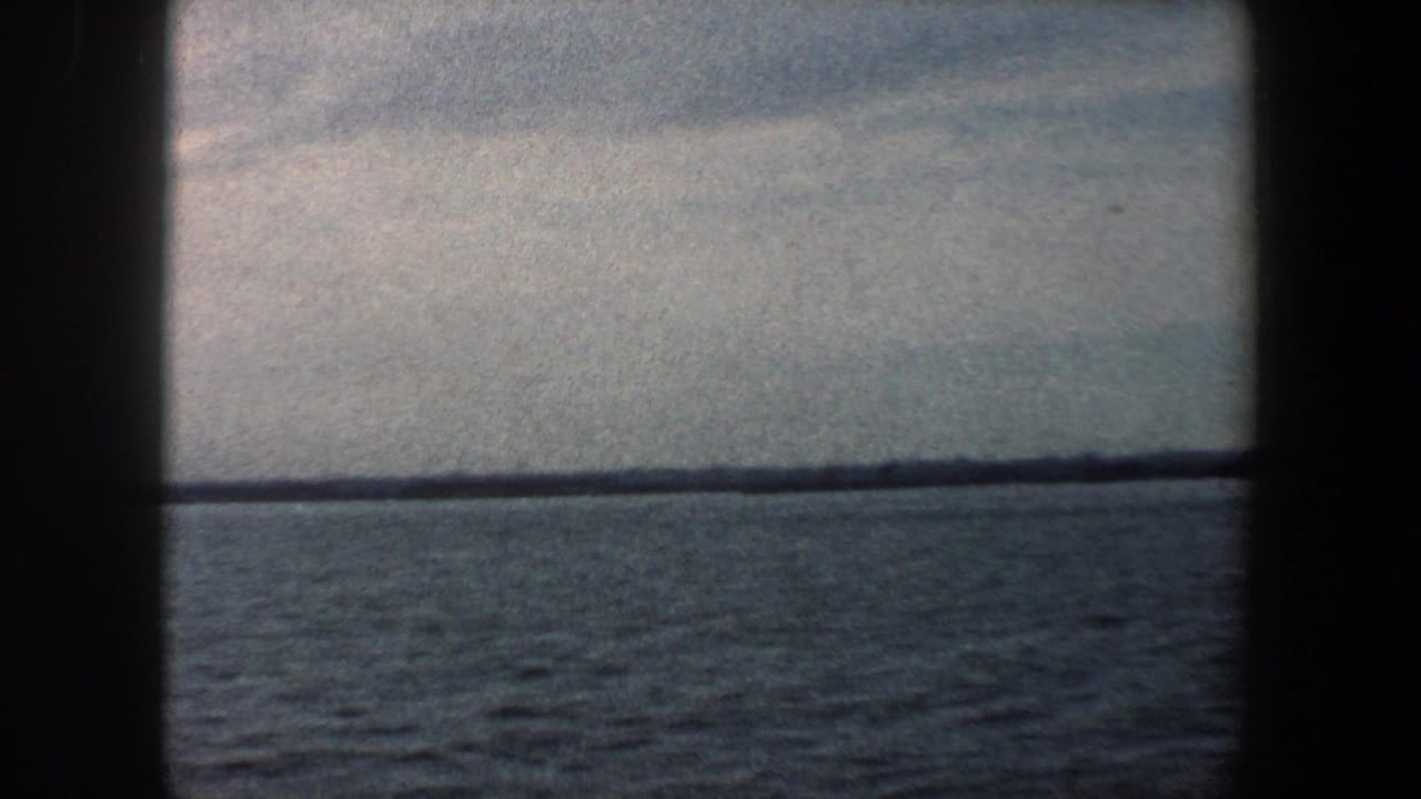 Open water and a thin distant shoreline seen through dark film-frame edges.