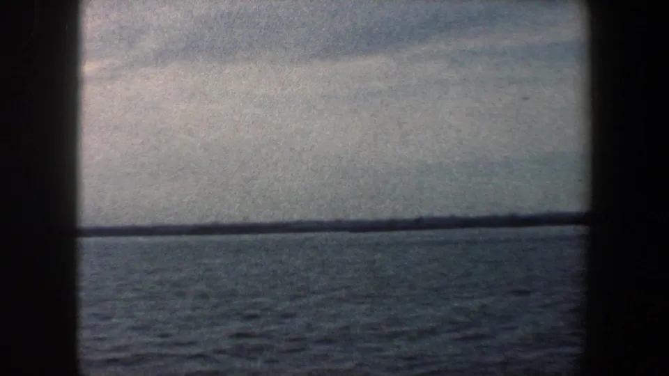 Distant New York Harbor shoreline across open water, framed by dark 8mm gate edges and a pale sky.