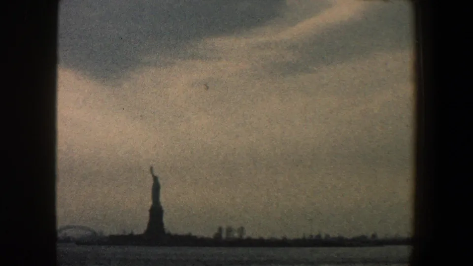 The Statue of Liberty appears as a distant silhouette across New York Harbor in 1960 home-movie footage.