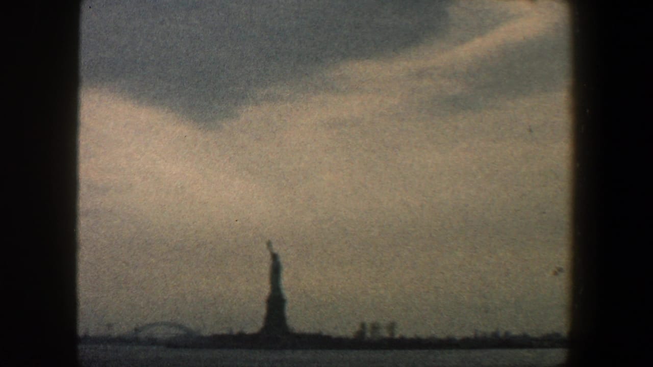 1960 8mm home-movie frame showing the Statue of Liberty in the distance across New York Harbor, bordered by dark vertical window framing.