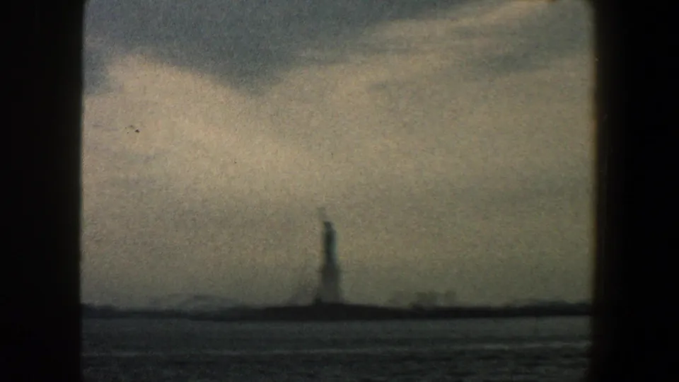 Distant 1960 New York Harbor view with the Statue of Liberty silhouetted against clouds and water in the foreground.