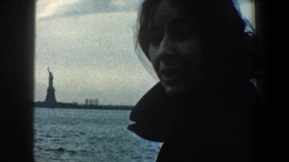 A silhouetted woman looks out from a vessel window toward the distant Statue of Liberty in 1960 New York Harbor home-movie footage.