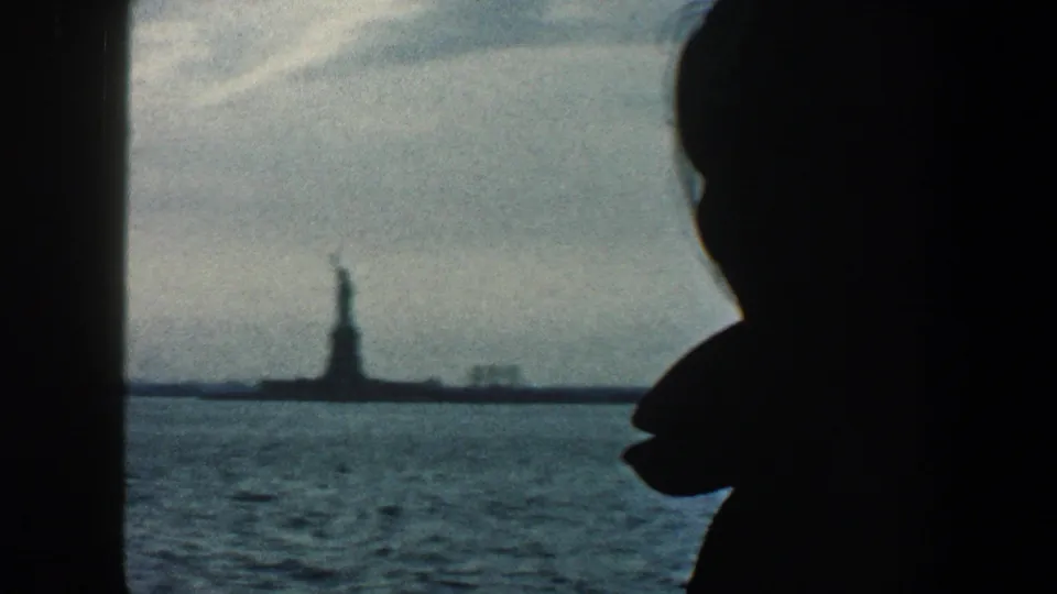 A dark side silhouette fills the foreground while the Statue of Liberty remains distant across the blue-gray harbor in 1960 New York City footage.