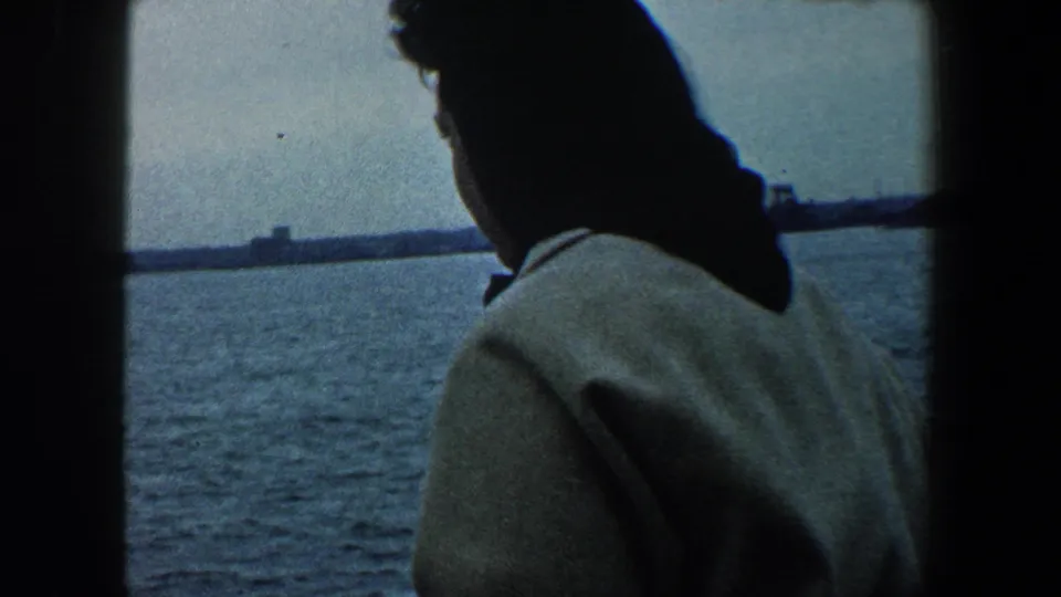 1960 New York City boat footage showing a woman from behind as she looks across harbor water toward the distant shoreline.