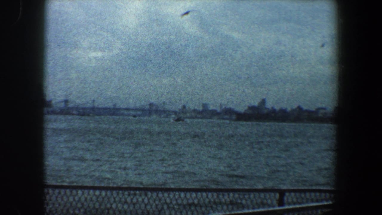 Distant New York City skyline across water with railing and dark film borders.