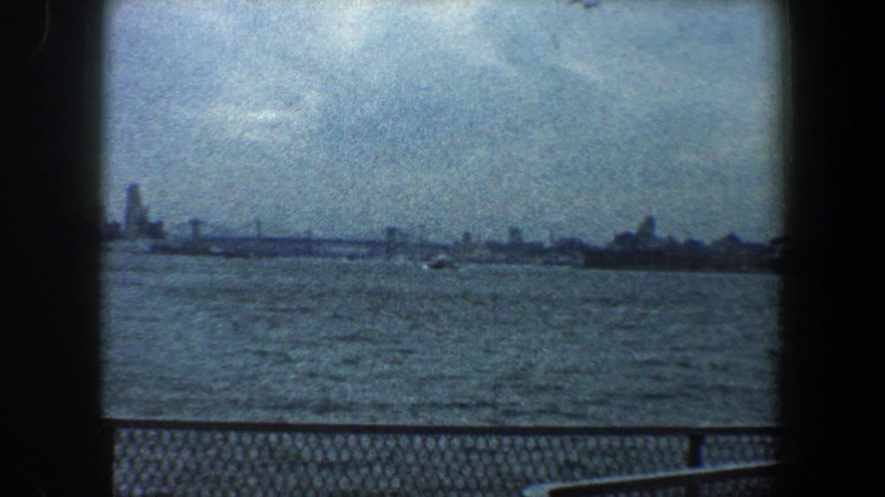 Hazy skyline across water with small boat and foreground railing.