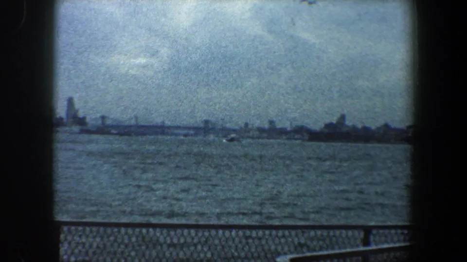 New York City skyline seen from across the water in 1960 8mm footage, with a small boat and railing in view.