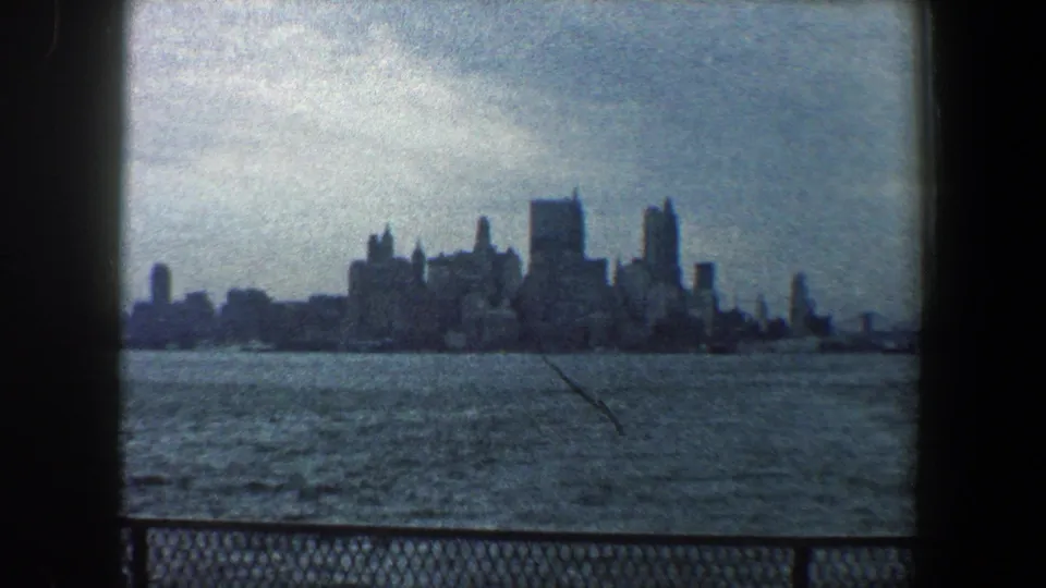 1960 8mm frame showing the New York City skyline from across the water, with railing at the bottom and a visible surface scratch.