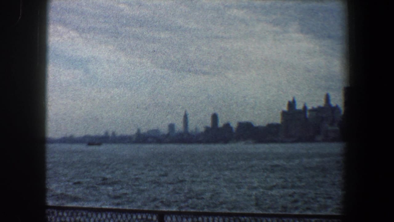 Wide waterfront view with distant skyline, rough water, and dark film borders.
