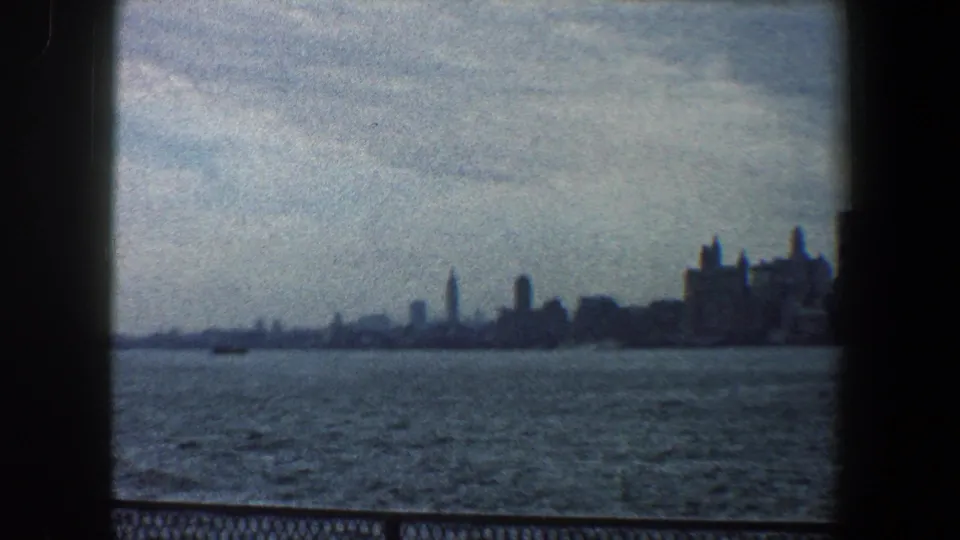 1960 New York City waterfront skyline appears far across the harbor, framed by dark 8mm gate edges and muted blue-gray exposure.