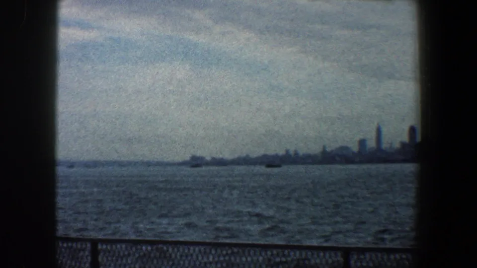 1960 8mm waterfront view of New York City, with open water in the foreground and a distant skyline compressed near the horizon.