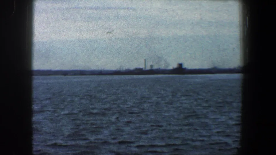 1960 New York City waterfront view showing choppy water, a low industrial horizon, and smokestacks in the distance.