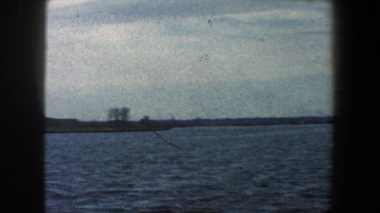 Distant harbor water and shoreline under cloudy sky with dark 8mm frame borders.