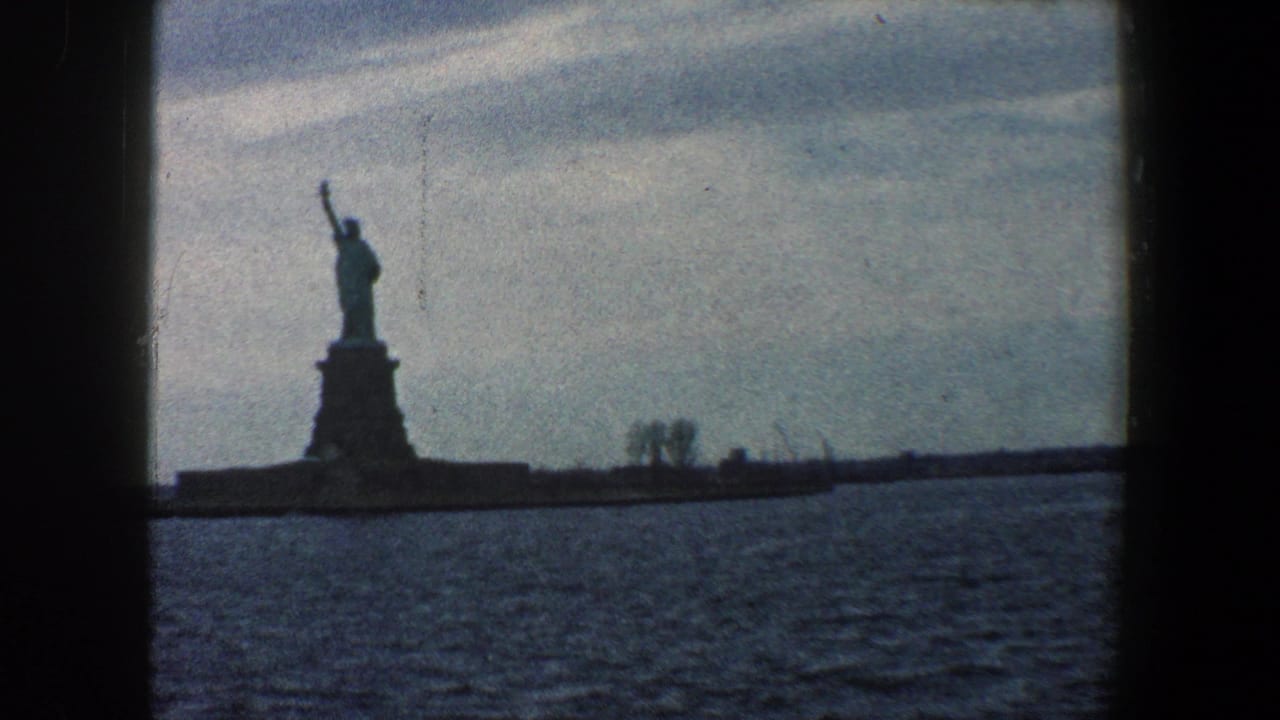 Statue of Liberty silhouetted across harbor water beneath a cloudy sky.