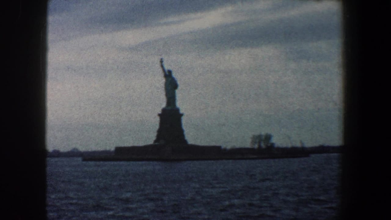 Statue of Liberty silhouetted across harbor water beneath an overcast sky.