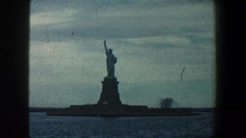 Final 1960 New York Harbor frame with the Statue of Liberty silhouetted at center, water below, clouds above, and dark home-movie framing.