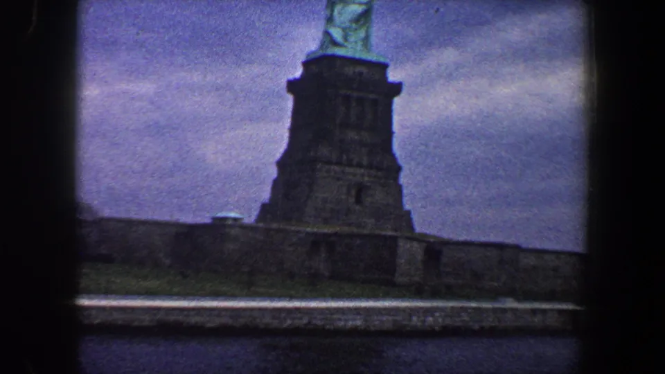 The final 8mm frame places the Statue of Liberty high in the composition, with the dark pedestal and base wall prominent below.