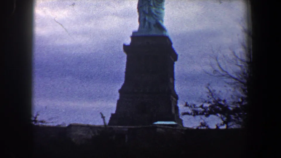 The camera holds on the Statue of Liberty pedestal and lower figure in a grainy 1960 New York City 8mm frame.